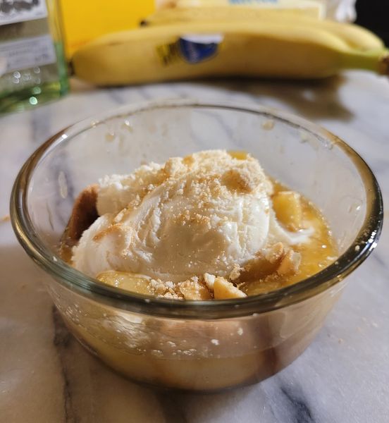 A serving of warm rum-fried bananas with syrup, ready to be topped with vanilla ice cream.