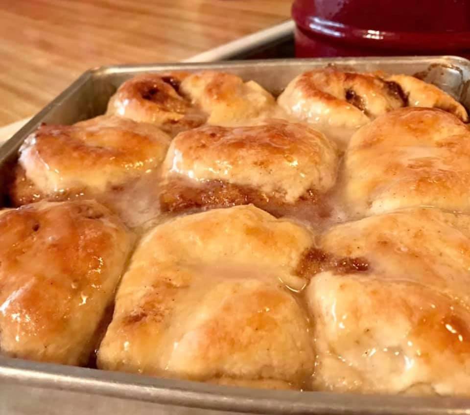 Pan of freshly baked cinnamon roll biscuits, golden brown with glaze pooling between them.