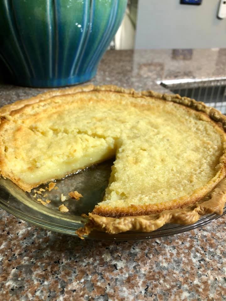 Buttermilk pie in glass pie dish with one slice missing, showcasing creamy texture.