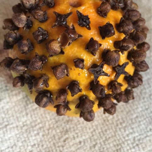 Homemade orange clove pomander with spiral clove design and red ribbon