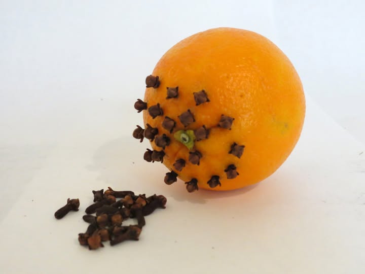Orange clove pomander drying on a kitchen counter with cinnamon sticks nearby.