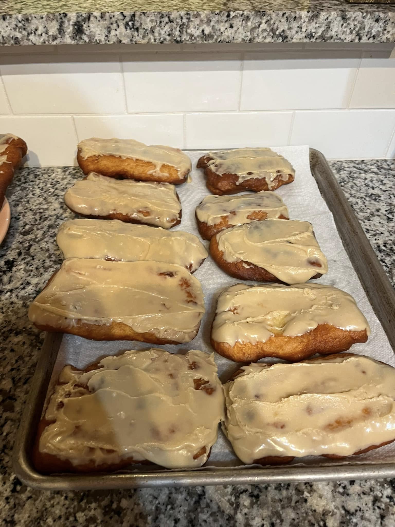 Maple bar donuts freshly glazed and cooling on a baking tray lined with paper towels.