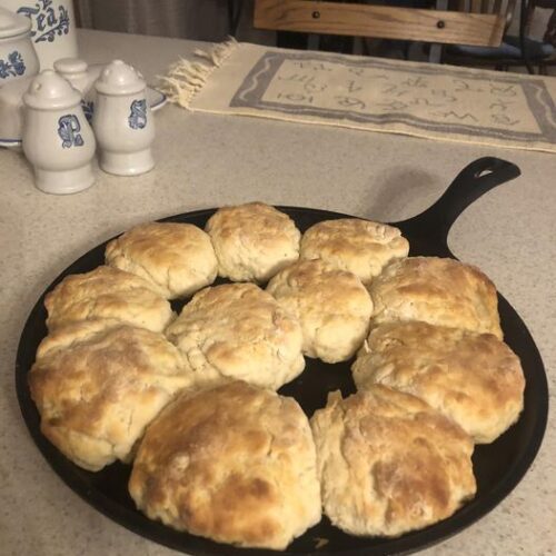 Homemade buttermilk biscuits baked in a cast iron griddle, arranged in a circle and golden brown.