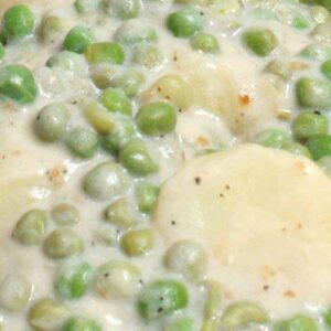 Close-up of creamy peas and potatoes with white sauce and bacon.