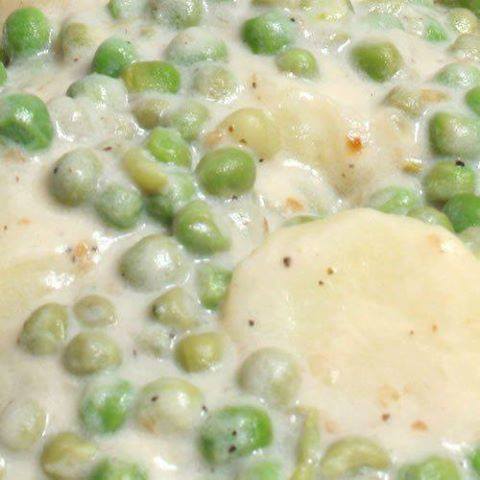 Close-up of creamy peas and potatoes with white sauce and bacon.