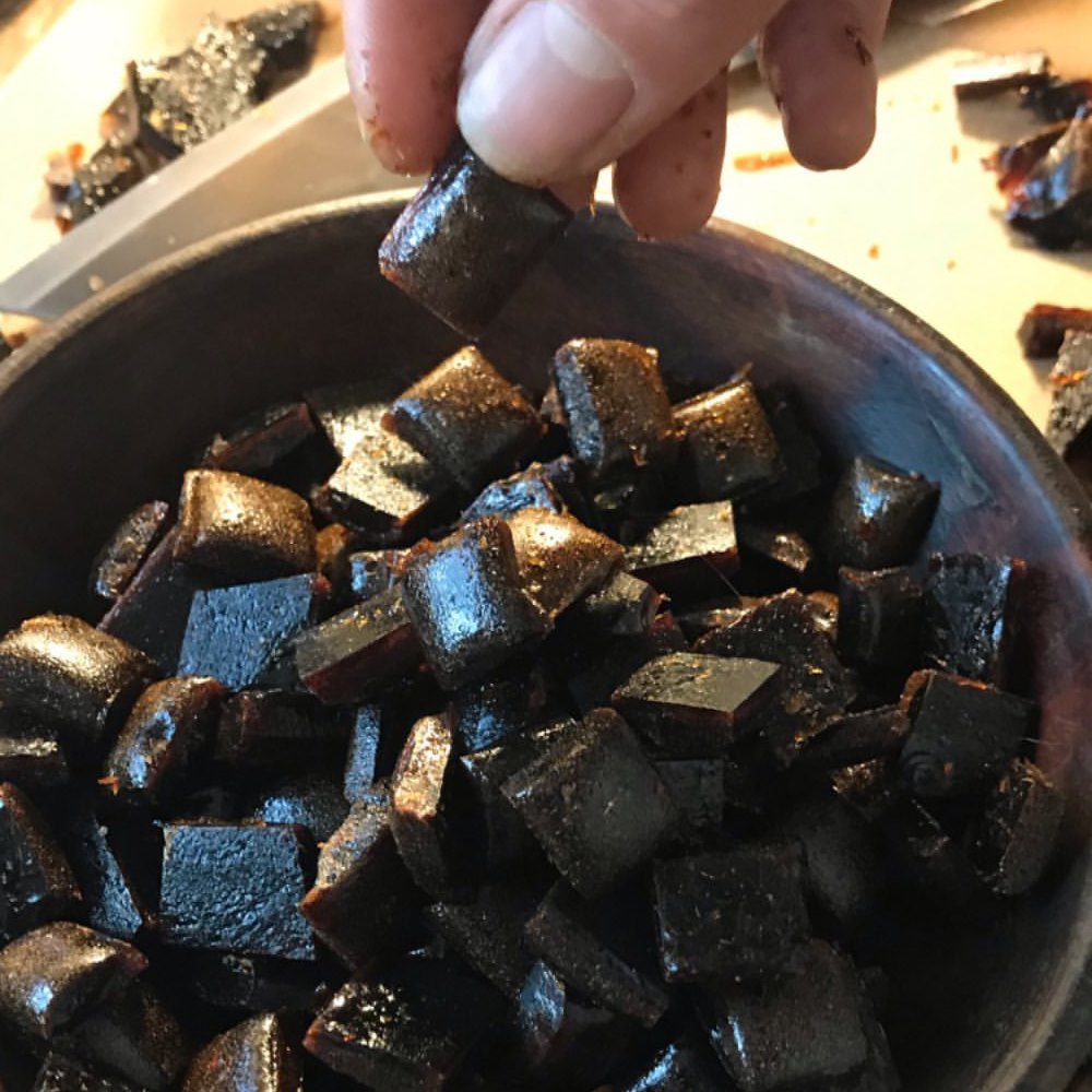 Close-up of dark, glossy horehound candies being handled and broken apart