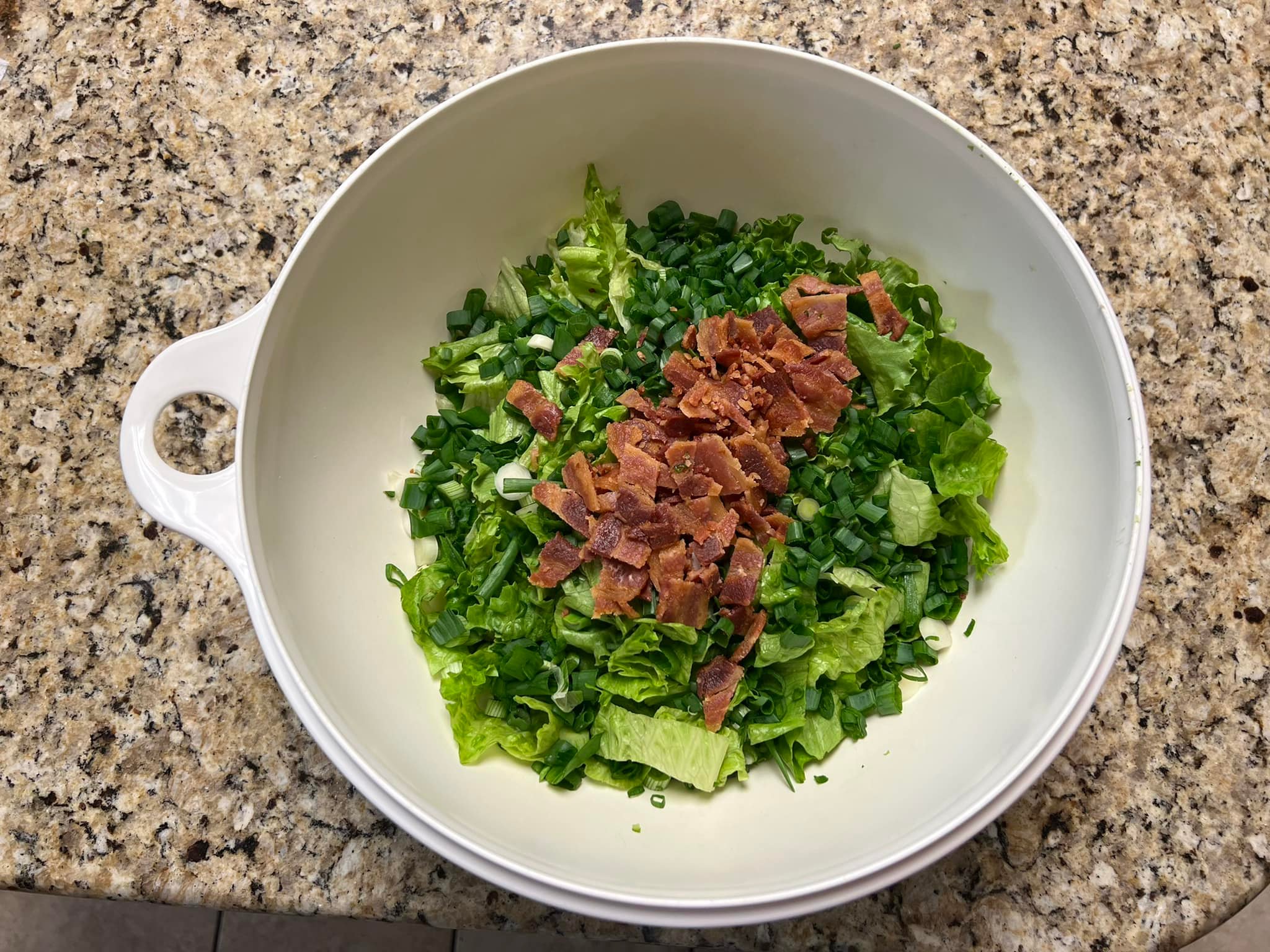Bowl of chopped lettuce topped with crispy bacon and green onions.