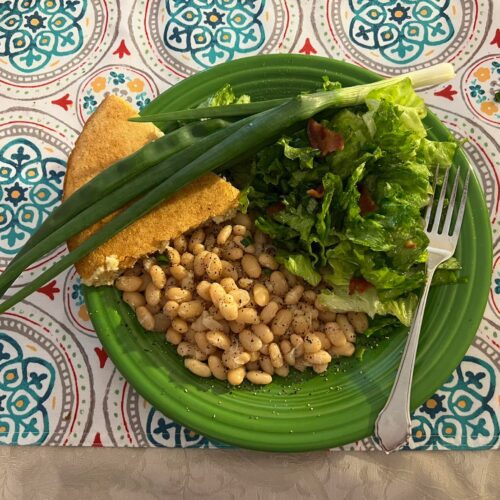 Southern dinner plate with wilted lettuce salad, white beans, cornbread, and green onions.