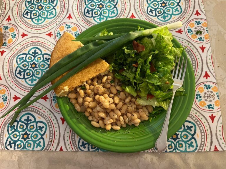 Southern dinner plate with wilted lettuce salad, white beans, cornbread, and green onions.