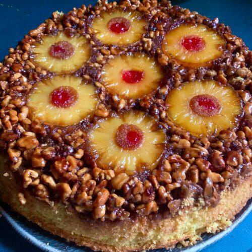 Candied walnut pineapple upside-down cake on a rustic plate, with golden pineapple rings, maraschino cherries, and a rich, crunchy brown sugar topping.