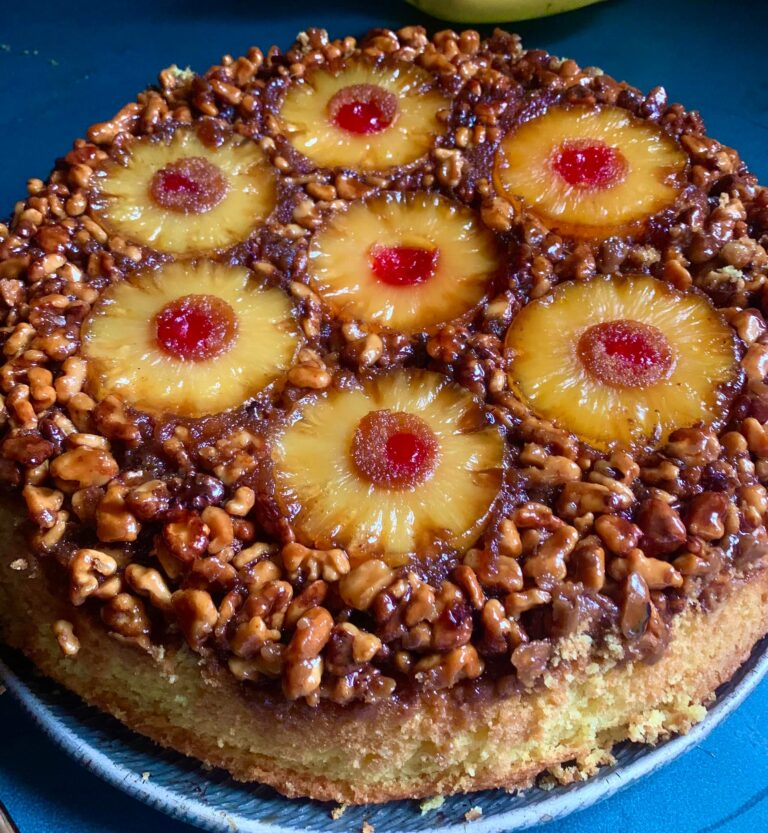 Candied walnut pineapple upside-down cake on a rustic plate, with golden pineapple rings, maraschino cherries, and a rich, crunchy brown sugar topping.