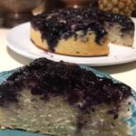 A slice of blueberry upside-down cake showing caramelized berry topping and fluffy vanilla crumb