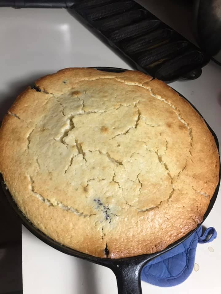 Whole blueberry upside-down cake flipped onto a white plate, topped with glistening berries.