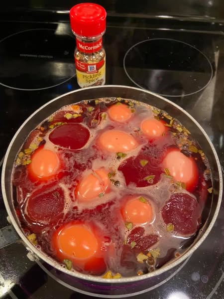 Pot of beets and peeled eggs simmering in pickling brine with visible spices.