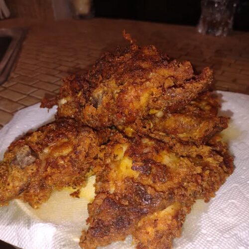 Pile of crispy golden brown mustard fried chicken draining on paper towels, close-up of textured crust.