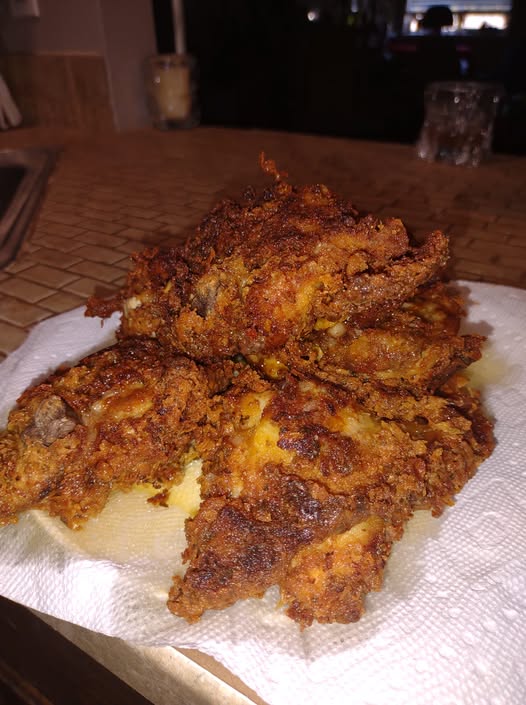 Pile of crispy golden brown mustard fried chicken draining on paper towels, close-up of textured crust.