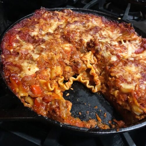 Cast iron skillet lasagna with bubbling cheese and visible pasta layers after serving a slice.