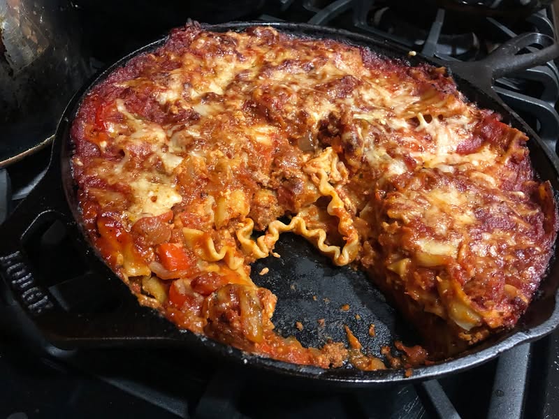 Cast iron skillet lasagna with bubbling cheese and visible pasta layers after serving a slice.