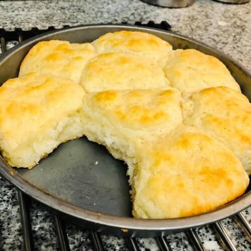 Fluffy homemade biscuits made with White Lily flour, baked golden in a round pan with one biscuit missing.