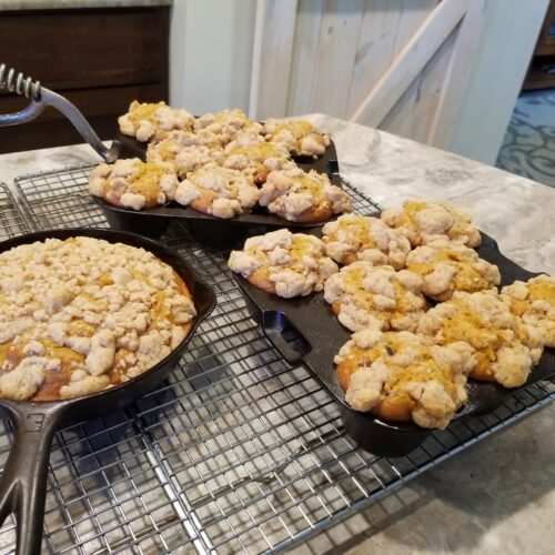 Pumpkin crumb muffins baked in vintage cast iron pans, topped with golden streusel and maple icing, cooling on a wire rack for a cozy fall breakfast