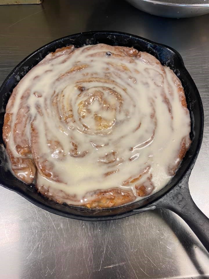 A cast iron skillet with a giant cinnamon roll swirled tightly and topped with creamy coffee-maple icing.