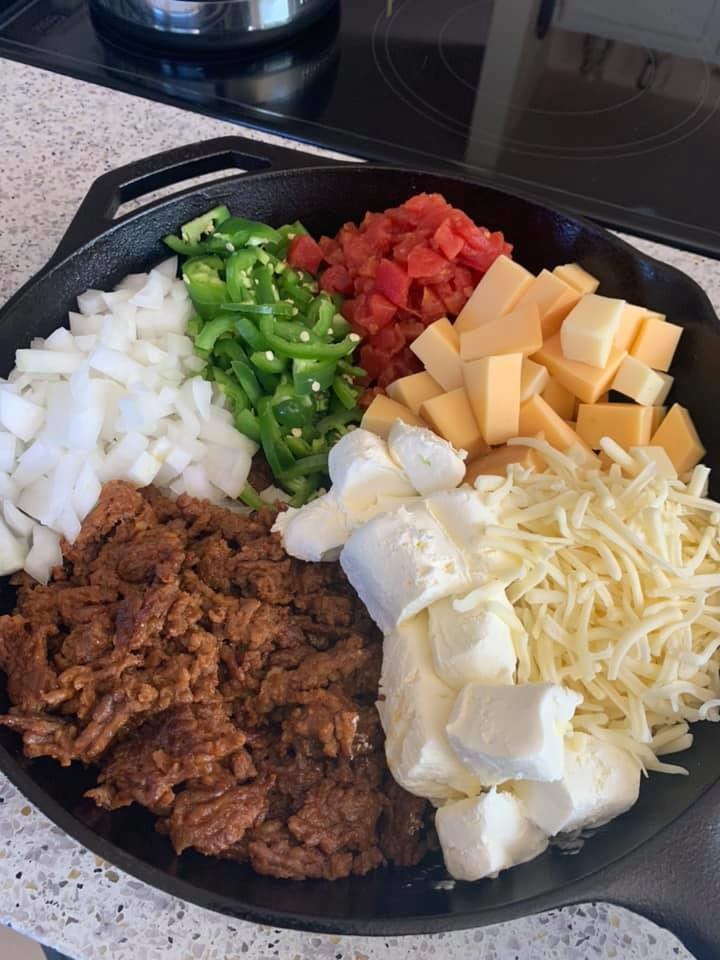 Chorizo, diced onion, jalapeños, Rotel, cubed smoked Gouda, shredded cheese, and cream cheese arranged in a cast iron skillet before cooking.