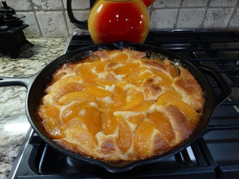 Golden brown peach skillet cobbler baked in a cast iron pan, topped with sliced canned peaches and served warm straight from the oven.