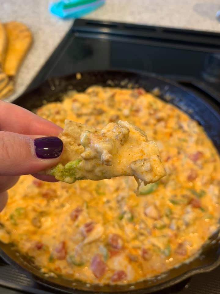 Tortilla chip scooping up a bite of creamy smoked queso with chorizo and jalapeños.
