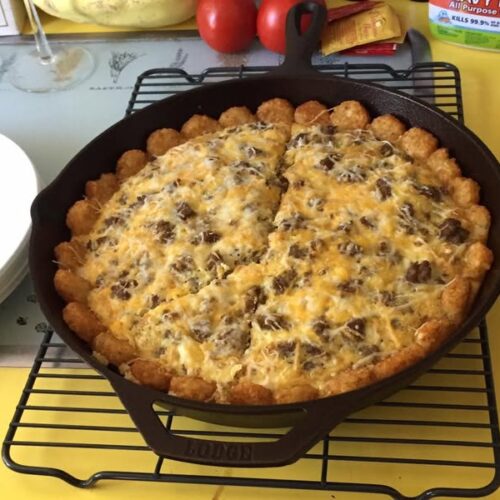A golden baked breakfast casserole in a cast iron skillet, made with hash brown rounds, sausage, eggs, and melted cheese.