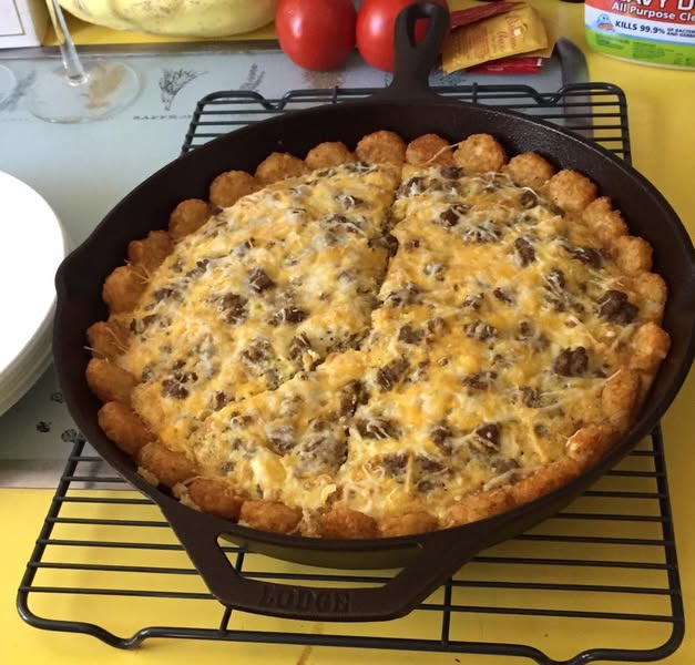 A golden baked breakfast casserole in a cast iron skillet, made with hash brown rounds, sausage, eggs, and melted cheese.