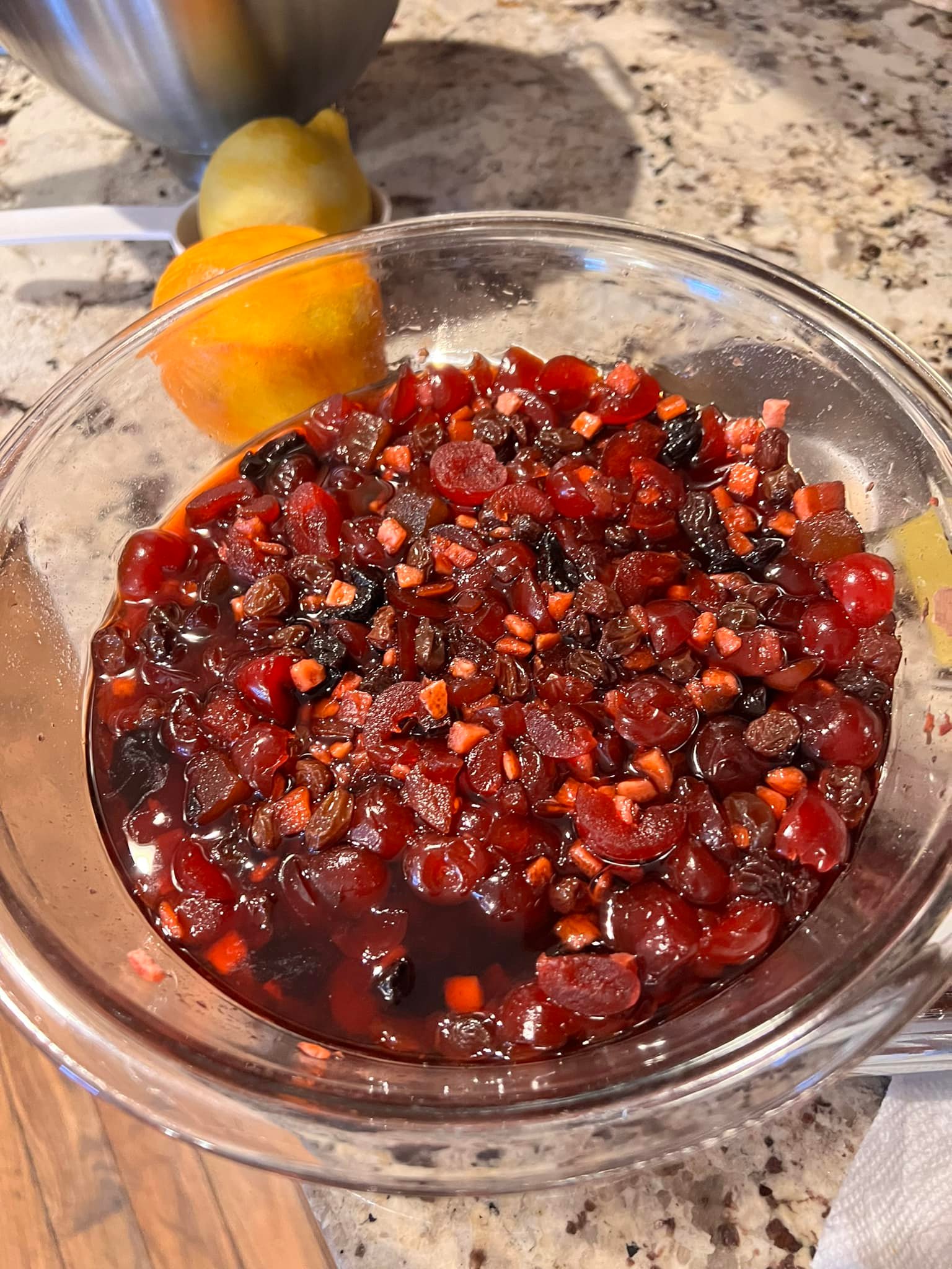 Mixing lemon zest, orange zest, and grated apple into homemade fruitcake batter in a stainless bowl.