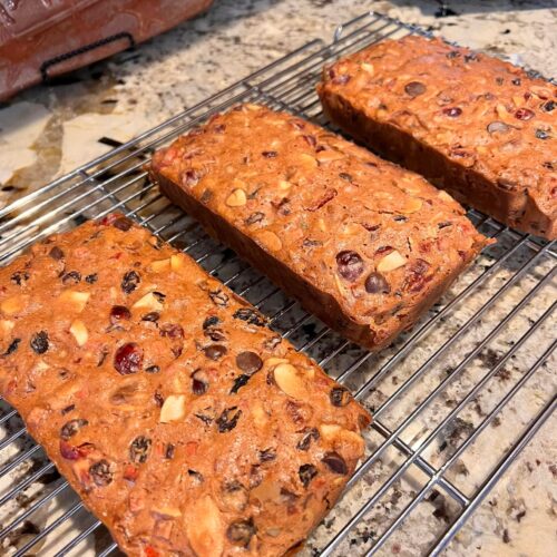 Homemade fruitcakes cooling on a wire rack after baking, with lots of nuts and dried fruit visible