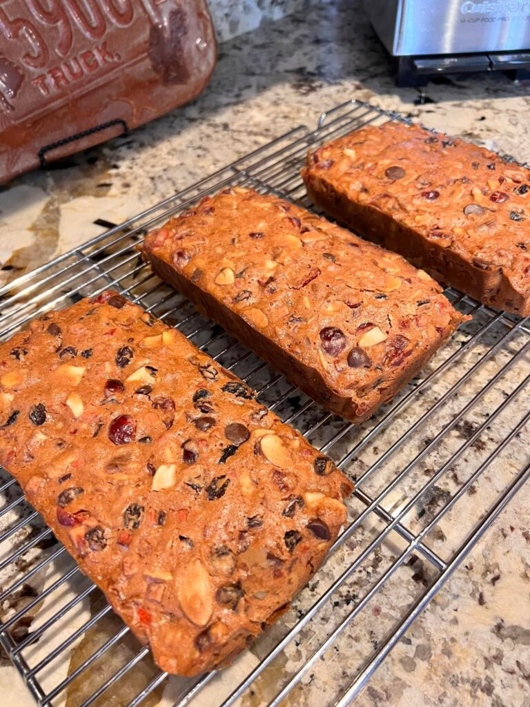 Homemade fruitcakes cooling on a wire rack after baking, with lots of nuts and dried fruit visible