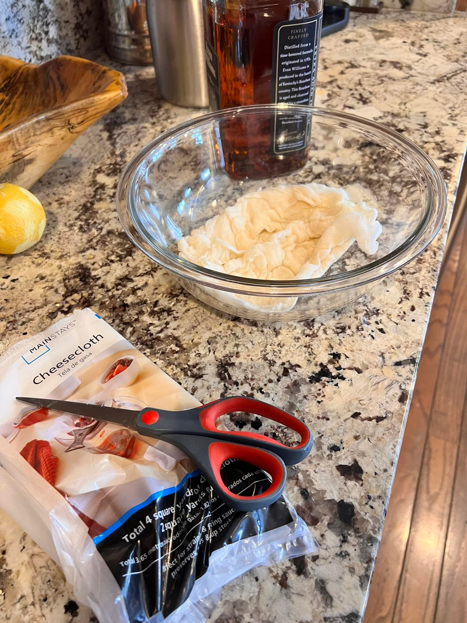 Cheesecloth soaking in brandy in a bowl, with scissors and bourbon ready to wrap homemade fruitcake