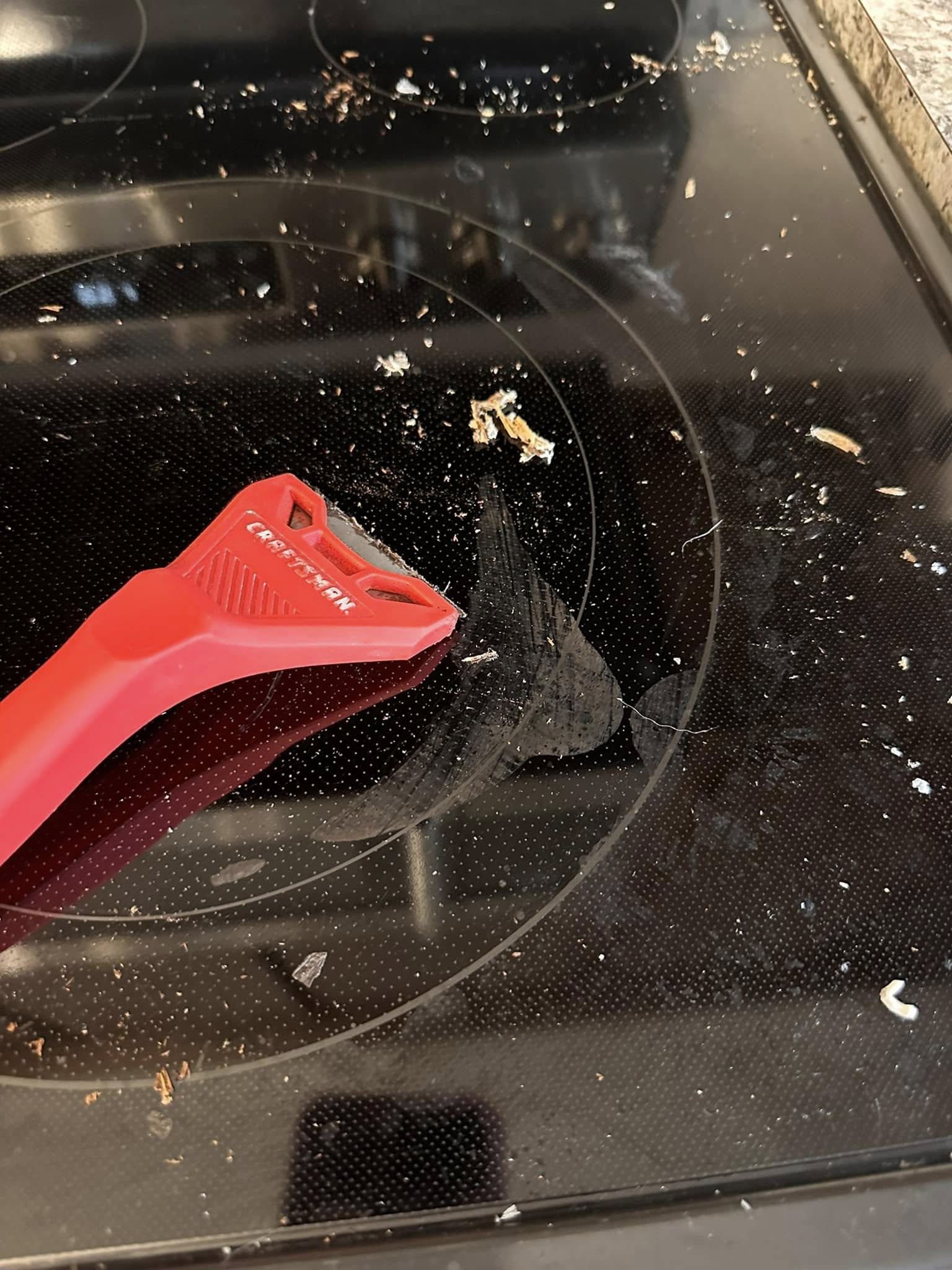 Dirty glass stove top with blade scraper for removing stuck-on mess