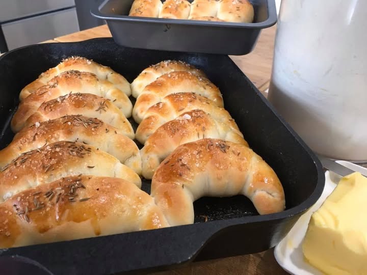 Freshly baked soft Hungarian kifli rolls in a cast-iron skillet, golden, butter-brushed & sprinkled with caraway seeds
