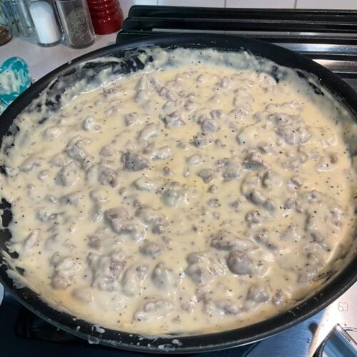 Creamy sausage gravy with evaporated milk simmering in cast‑iron skillet.