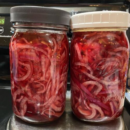 Vibrant quick pickled red onions packed tightly in a mason jar, layered with beet ribbons