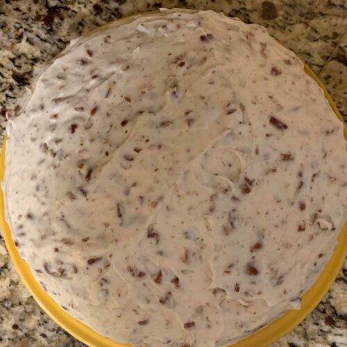 Cream cheese pecan frosting covering carrot cake