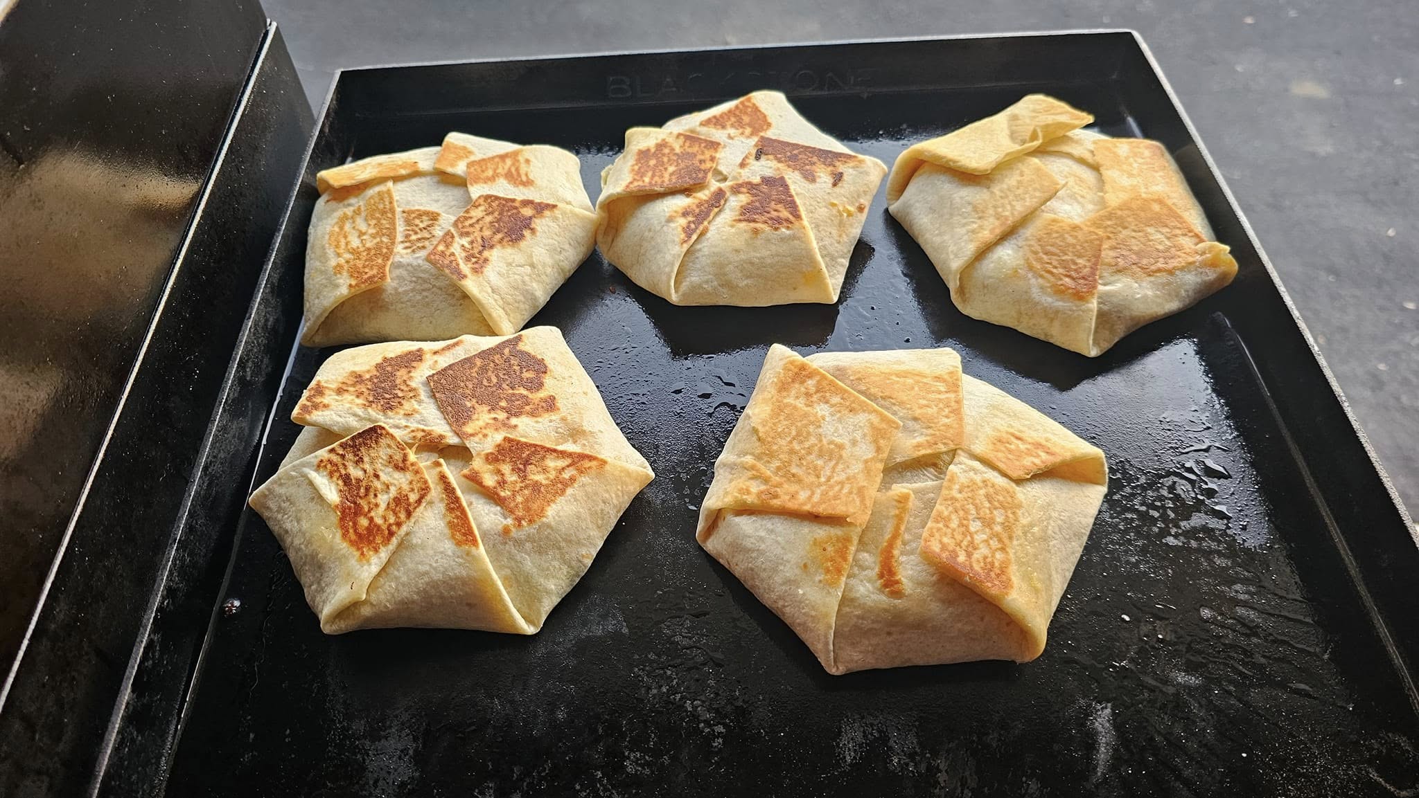Five crunchwrap supremes crisping on outdoor griddle.