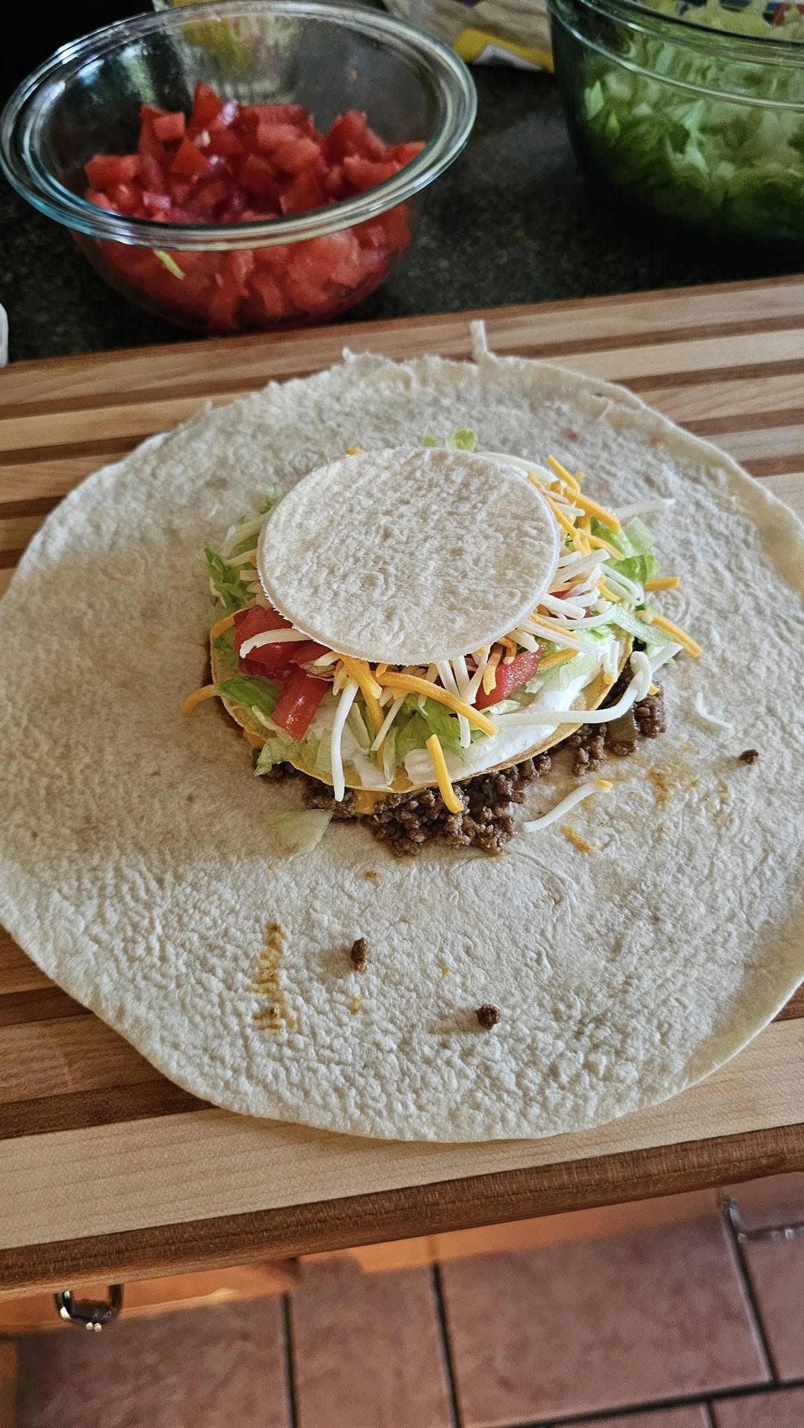 Taco meat, tostada, sour cream, veggies stacked on large tortilla