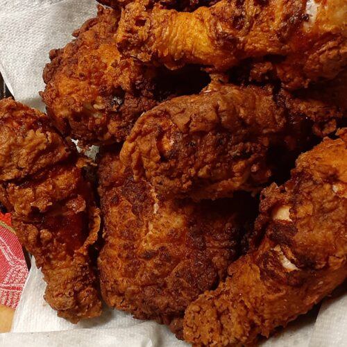 Pile of crispy buttermilk fried chicken drained on paper towels – golden brown perfection