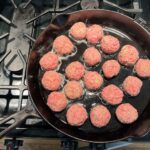 raw meatballs sizzling in cast iron skillet with oil
