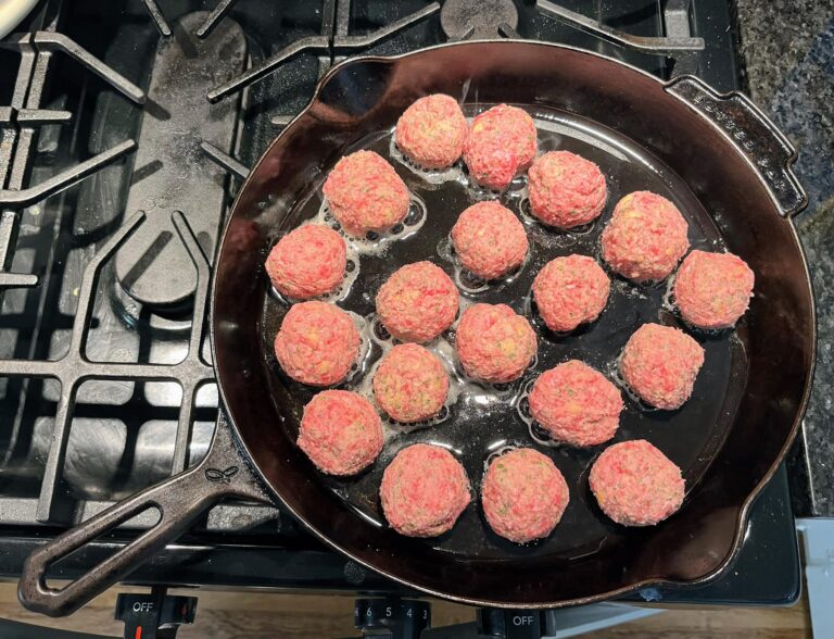 raw meatballs sizzling in cast iron skillet with oil