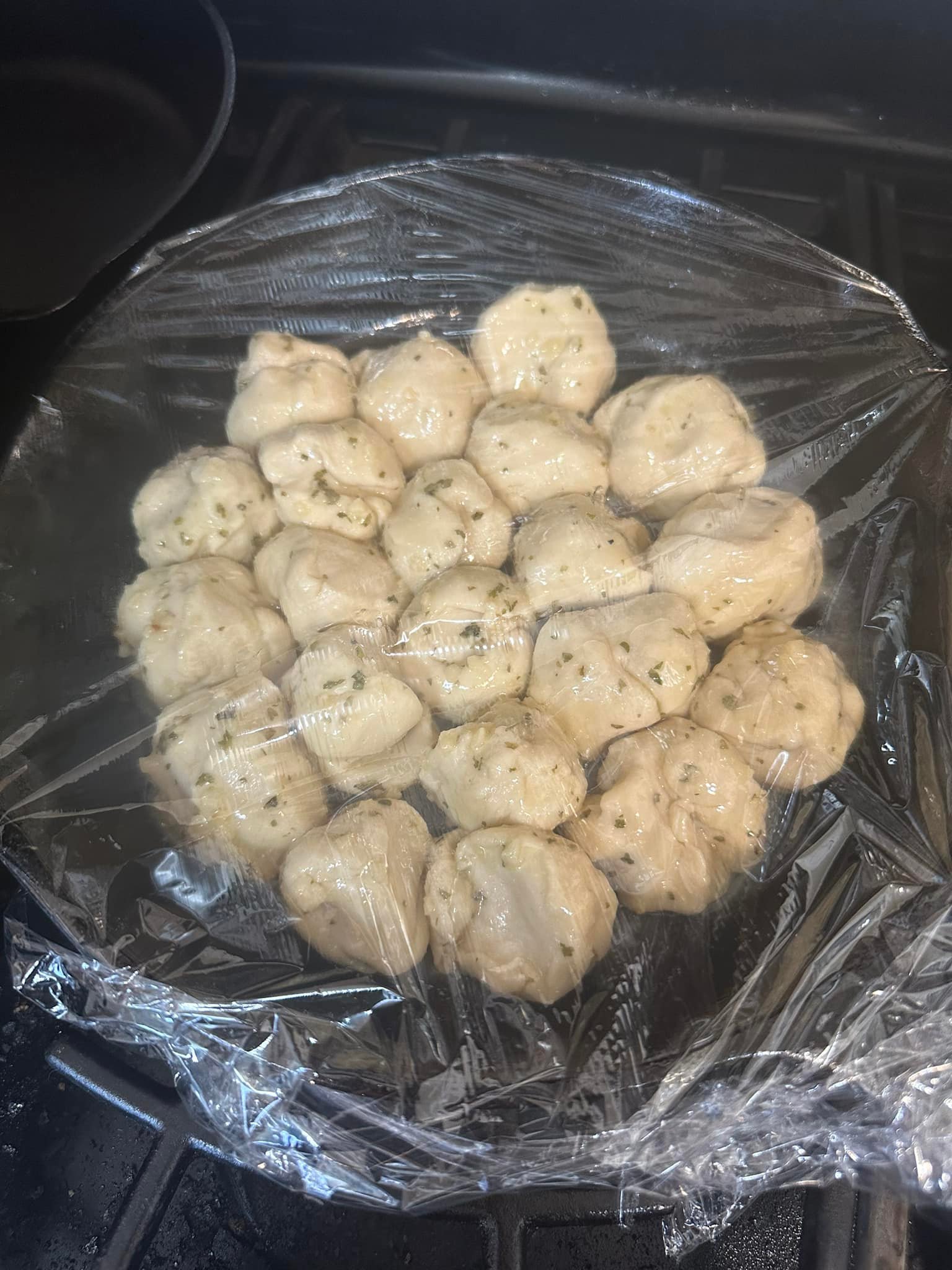 cast iron skillet filled with garlic knot dough balls rising under plastic wrap