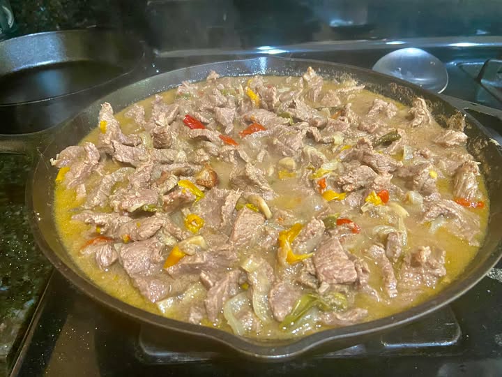 cast iron skillet filled with beef strips, peppers, and onions for homemade Philly cheesesteak