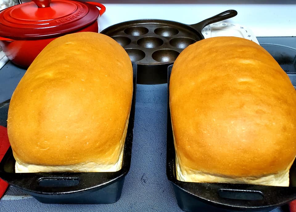 freshly baked golden brown sandwich loaves in cast iron pans