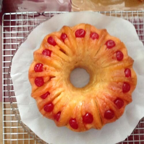 : Pineapple upside down Bundt cake flipped onto plate with cherries and pineapple