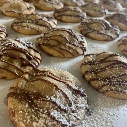 Snickers Surprise Cookies drizzled with chocolate and powdered sugar