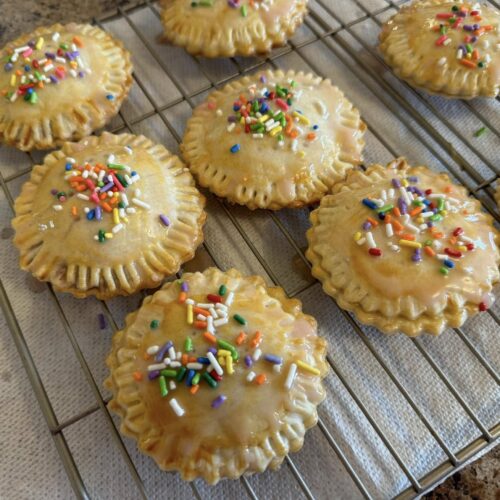 Heart-shaped pop tarts with pink icing and colorful sprinkles on cooling rack